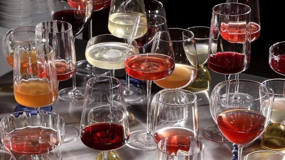 Twenty wine glasses filled with an array of red, white, and orange wines.
