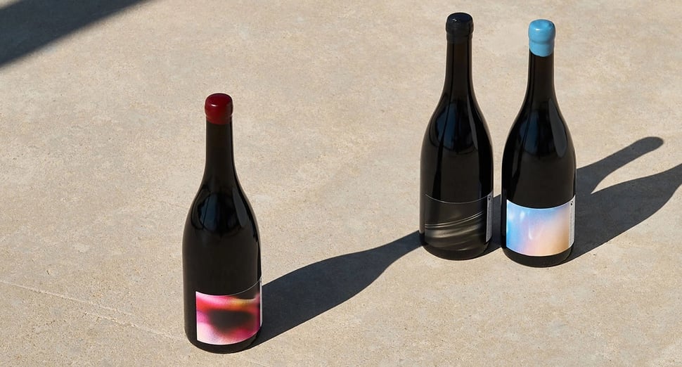 Three wine bottles on concrete ground with abstract logos in the colors red, black, and blue