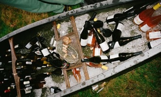 Around 50 various bottles of wine sitting in ice placed within a small metal boat sitting on the grass.